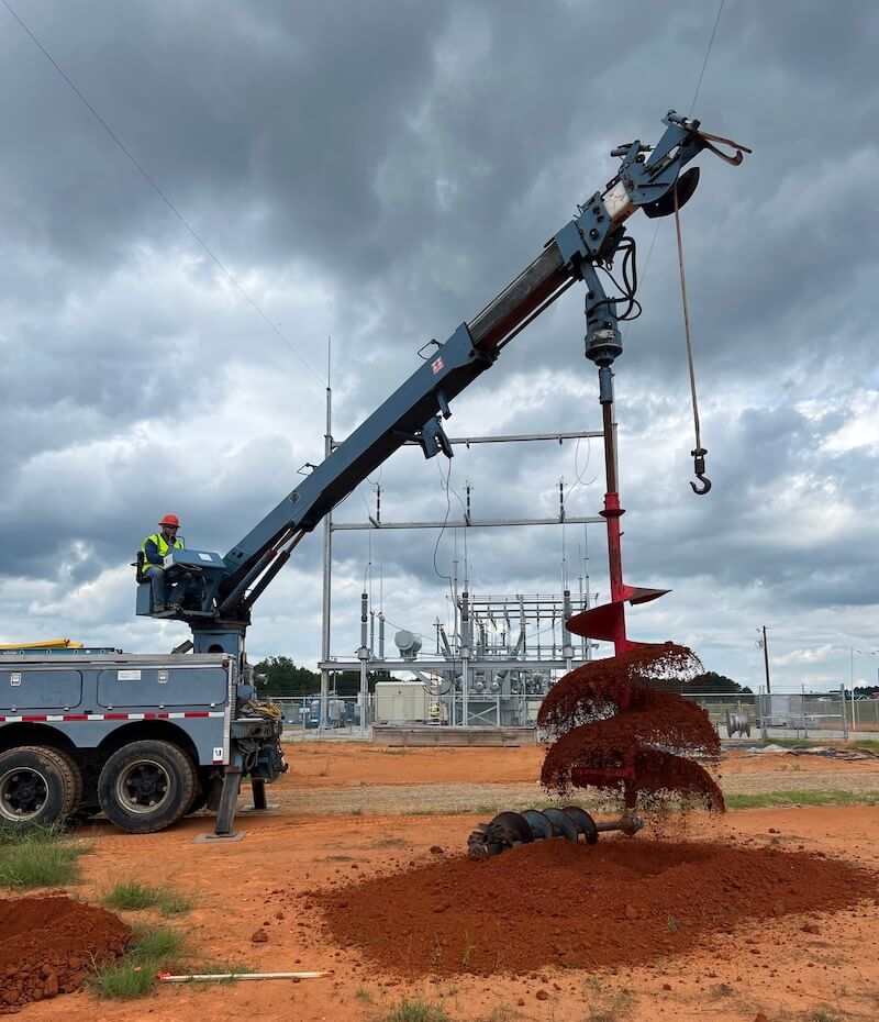 Clouds rolling in overhead as a large post hole digger works