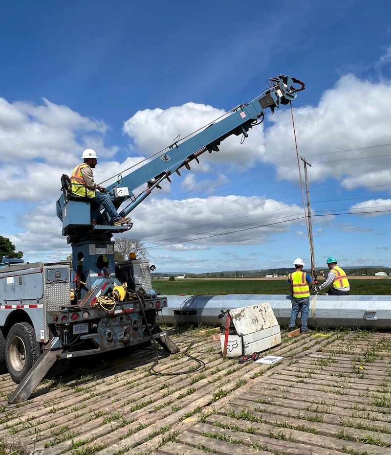 Crane truck operator and power line workers preparing to move a metal utility pole