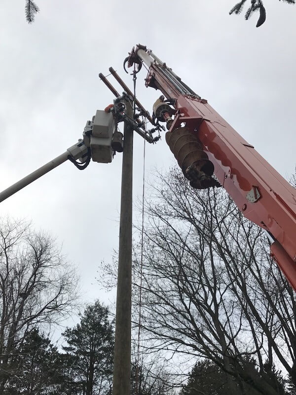 Installation of a distribution telephone pole with man basket and crane shown